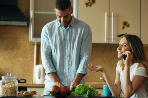 Attractive couple in the kitchen early morning. Beautiful girl chatting phone while her boyfriend cooking breakfast at home