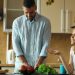 Attractive couple in the kitchen early morning. Beautiful girl chatting phone while her boyfriend cooking breakfast at home