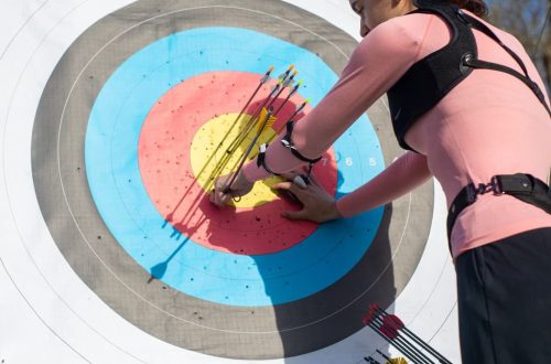 A female archer inspects arrows on a target after a shooting session outdoors.