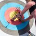 A female archer inspects arrows on a target after a shooting session outdoors.